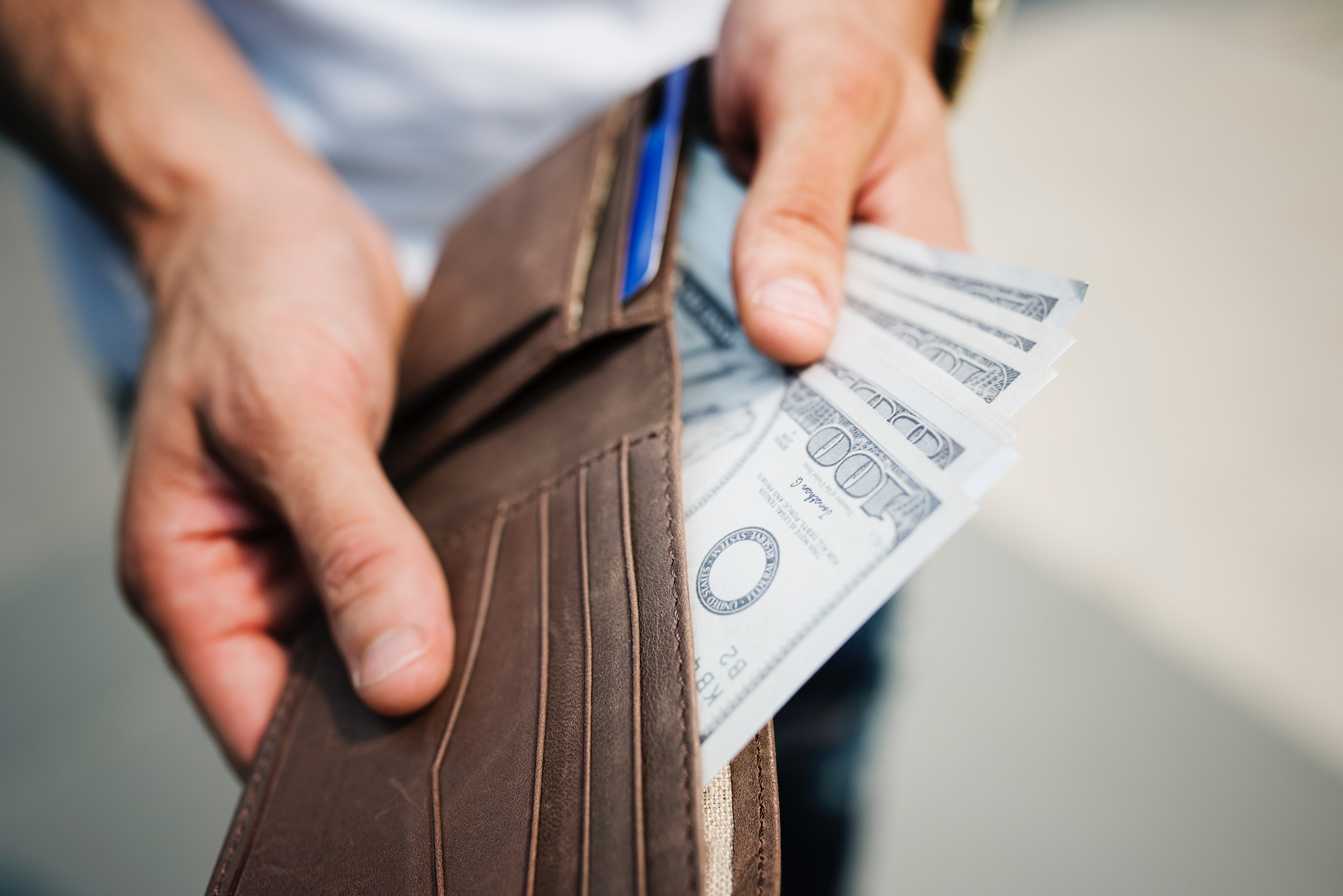 man holding brown leather bi fold wallet with money in it